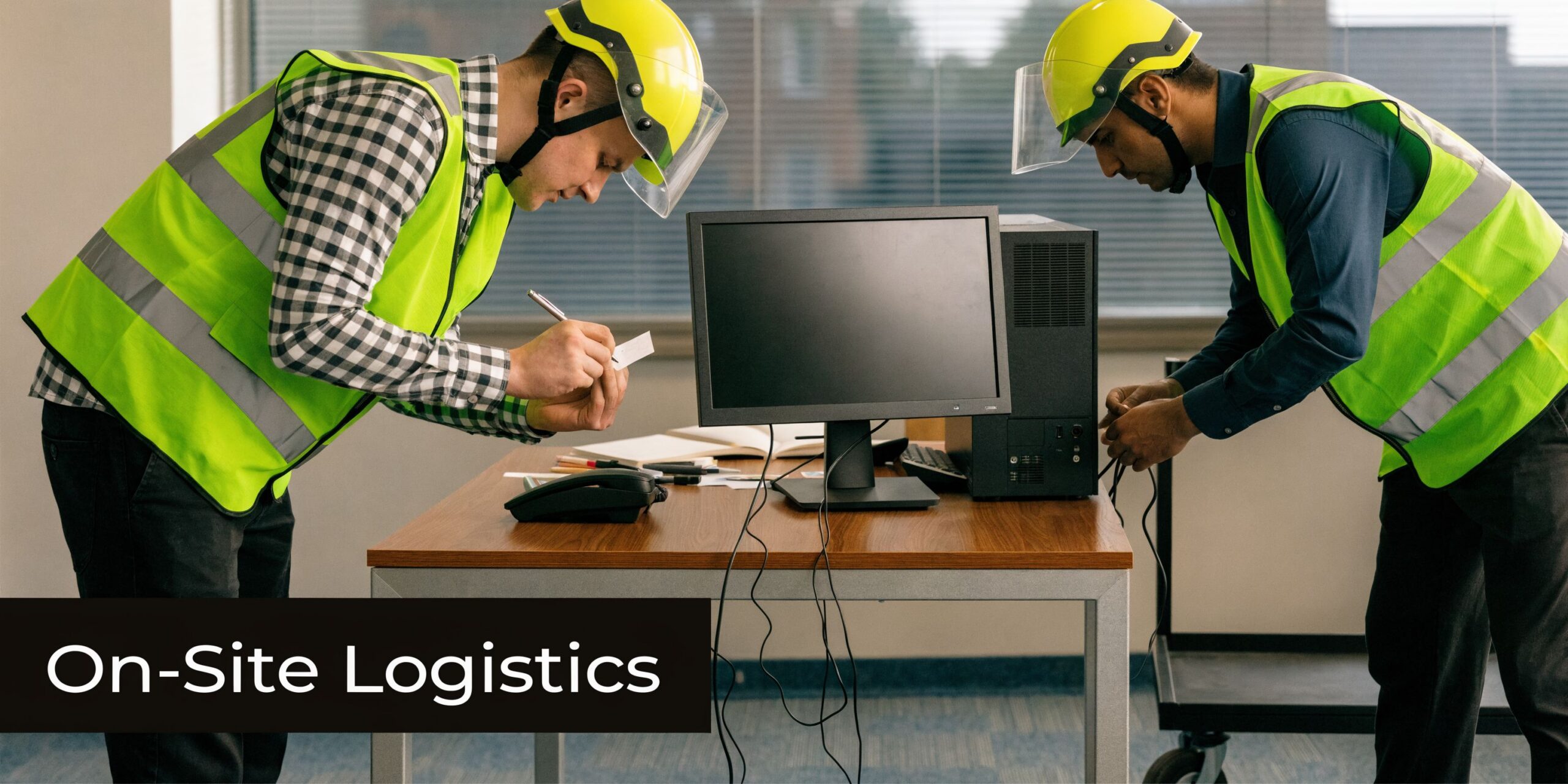 Two technicians wearing safety gear and hard hats inspecting computer equipment in a modern office workspace.