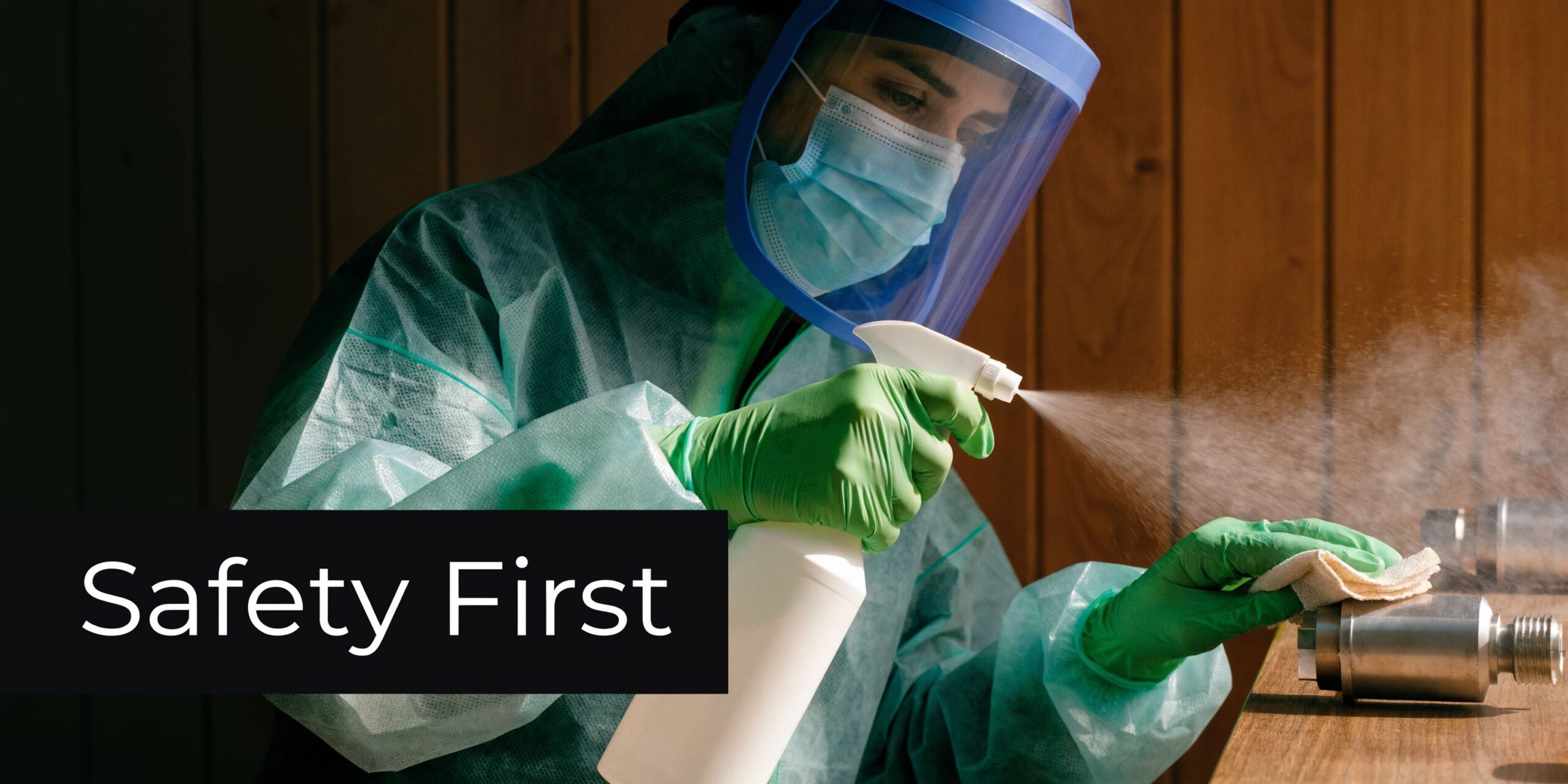 A professional in full PPE gear cleaning a metallic piece of lab equipment with disinfectant spray.